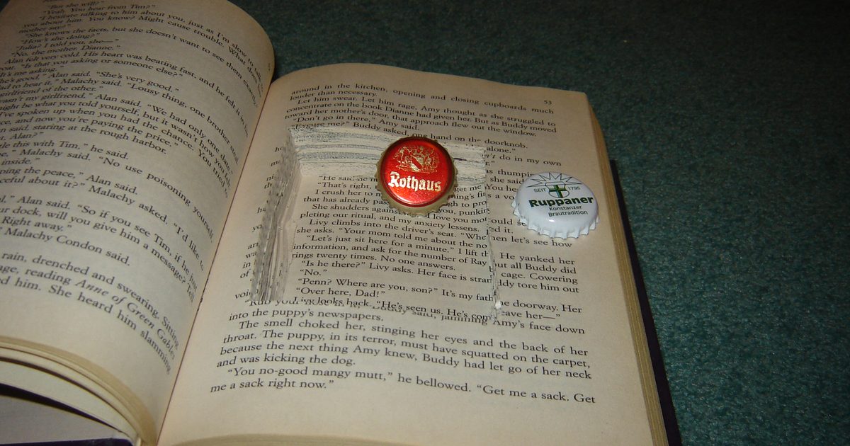 Open hardcover book with a hidden storage cavity cut into its pages, holding two bottle caps