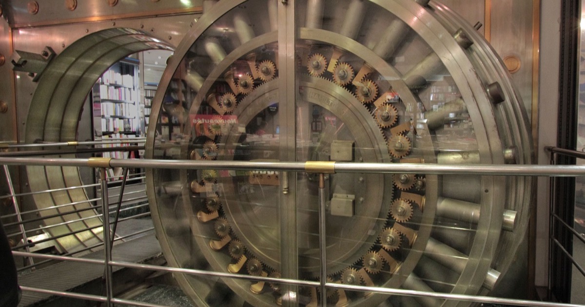 Circular bank vault door with exposed locking gears behind a railing