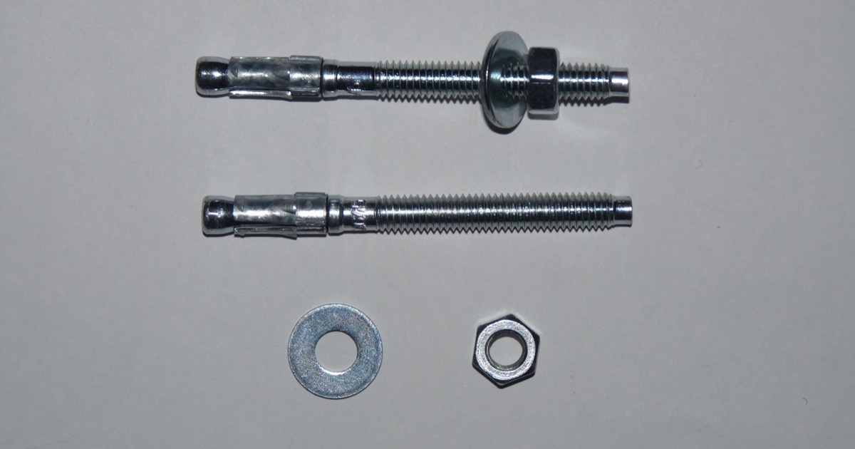 Two steel wedge anchor bolts with a washer and hex nut on a gray surface