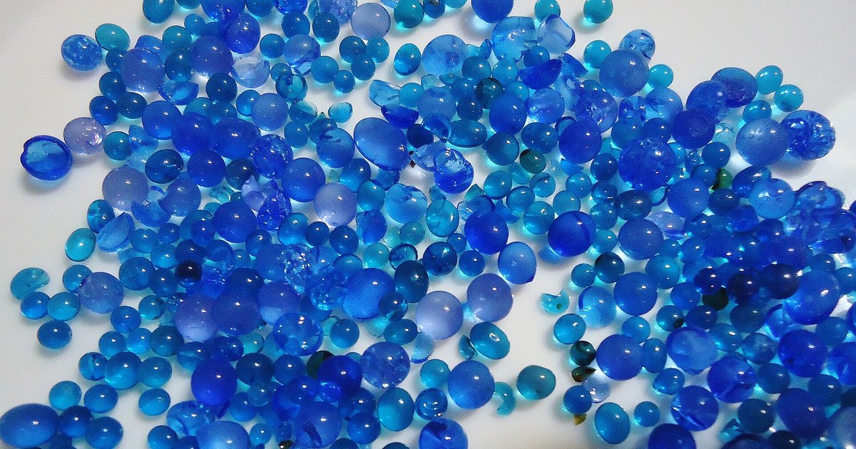 Loose blue indicating silica gel desiccant beads spread across a white surface